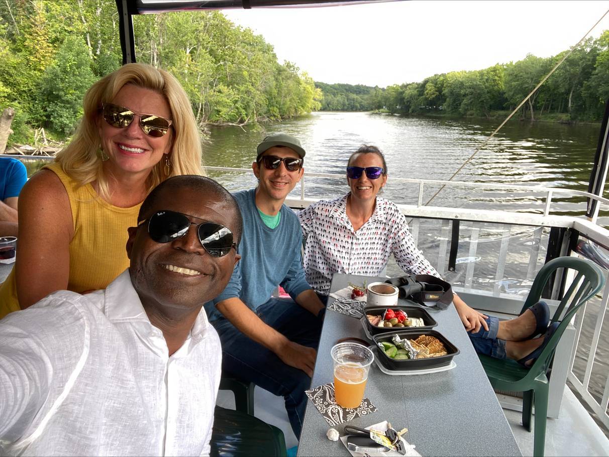 a photo of people sitting at a table eating and smiling for a picture on a riverboat deck